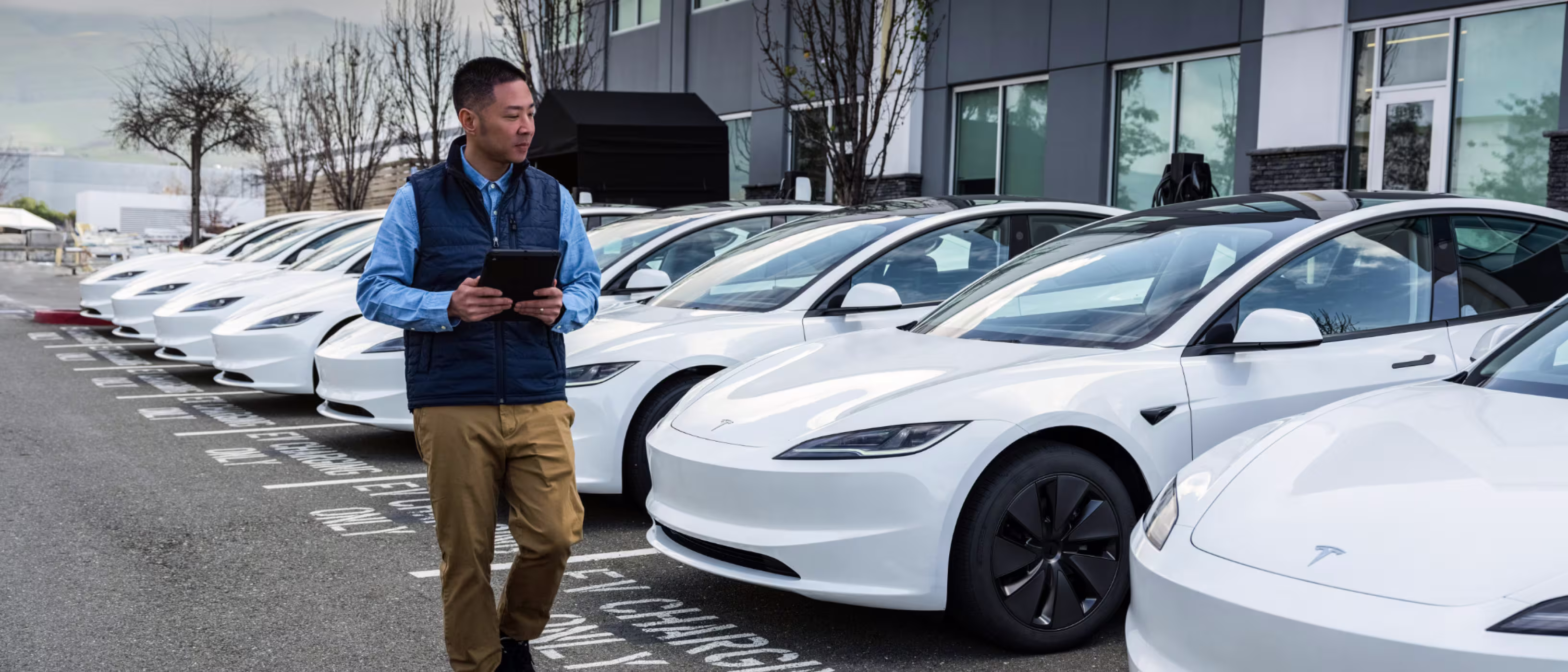 Servis otoparkında sıraya dizilmiş beyaz Tesla'lar ve elinde tablet olan görevli
